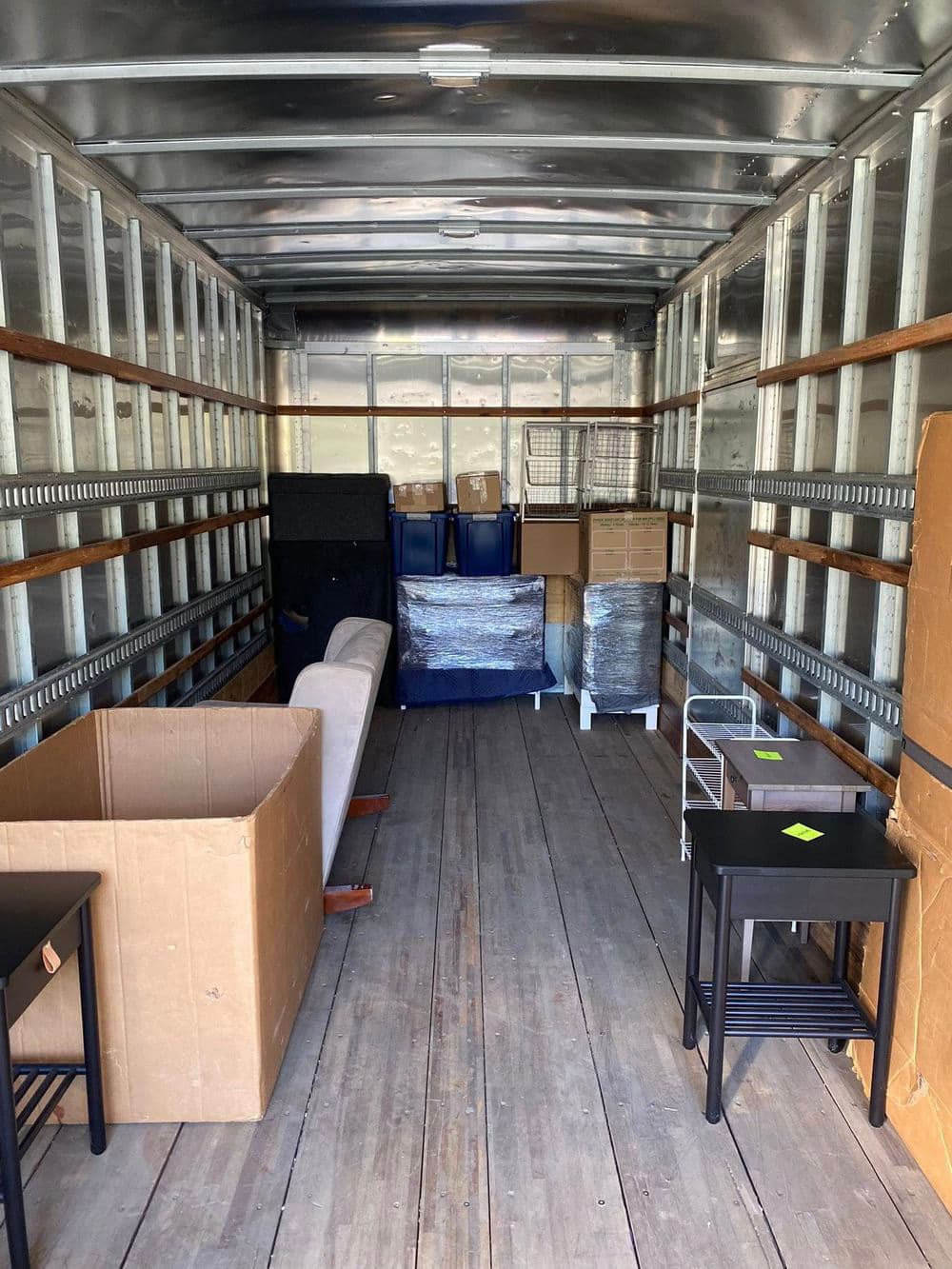 Interior of a moving truck with packed furniture, including boxes, tables, and chairs.