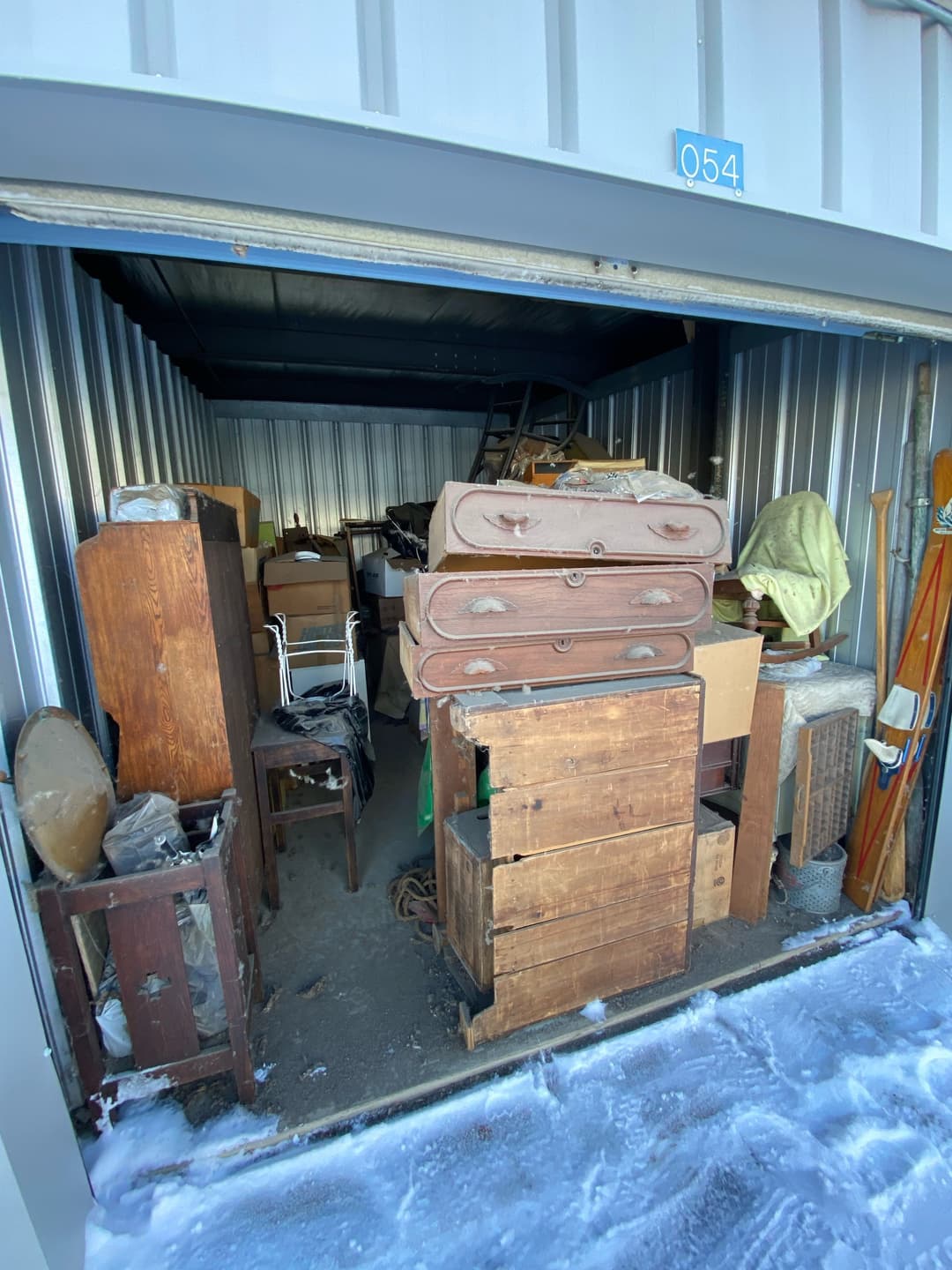 Cluttered storage unit filled with wooden furniture, boxes, and miscellaneous items.